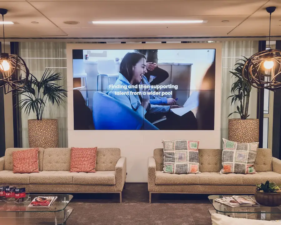 A large-format digital signage screen integrated into a modern corporate lounge area