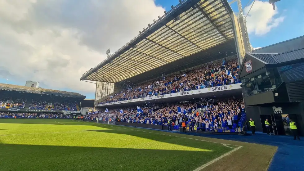A packed football stadium stand showing digital perimeter boards and large-scale IPTV screens for live event-driven content delivery.